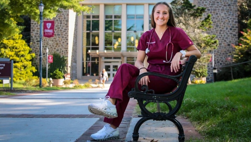 Nursing student sits on bench on college campus.