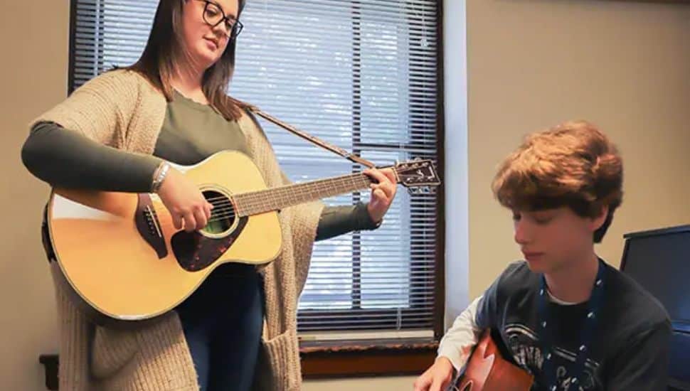 A music instructor plays guitar while guiding a student during a lesson at the Immaculata University Community Music School.