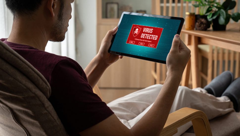 Man viewing a tablet screen displaying a red “Virus Detected” warning, a common tactic used in tech support scams.