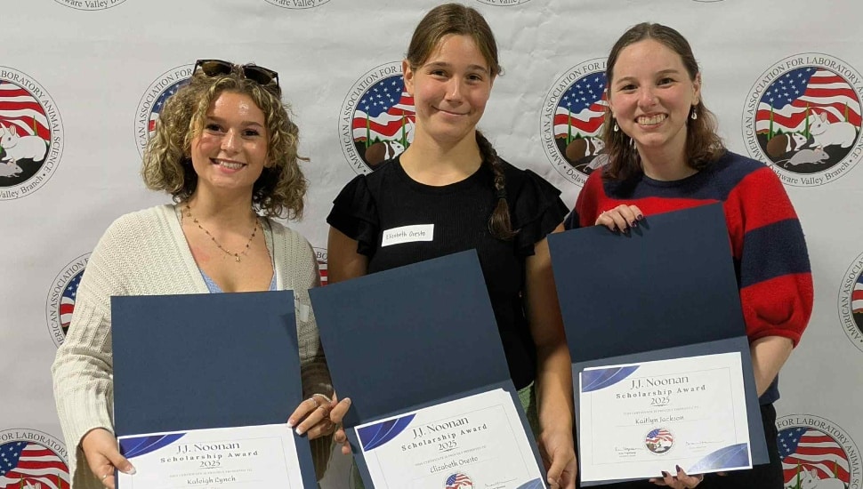 Three female college students receive certificates of achievement.