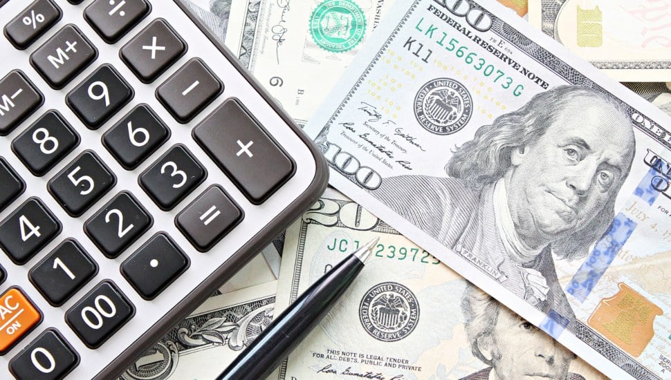 Cash on a table next to a pen and a calculator.