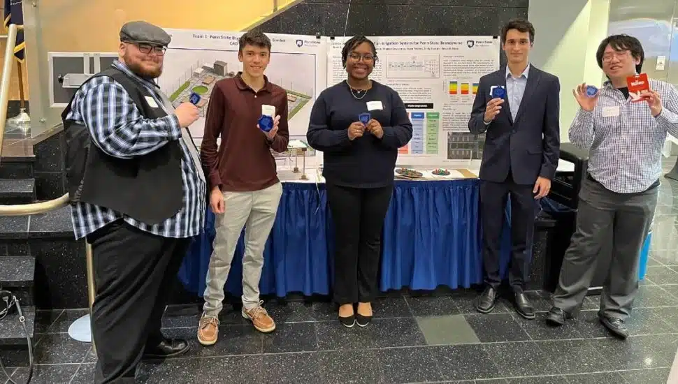 Five Penn State engineering students with Cornerstone Engineering Design in front of a table at a public event.