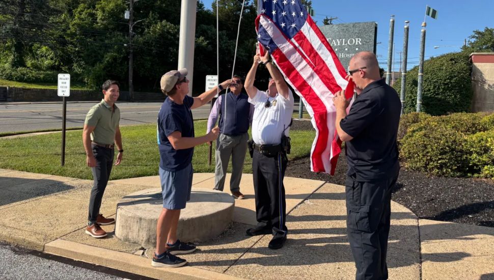 A flag is raised Tuesday at Taylor Hospital in Ridley Park by Ridley Park Police Chief William Thomas with the new owners of the hospital.