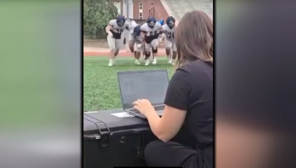 A person at a laptop watching football player in the distance on the field.