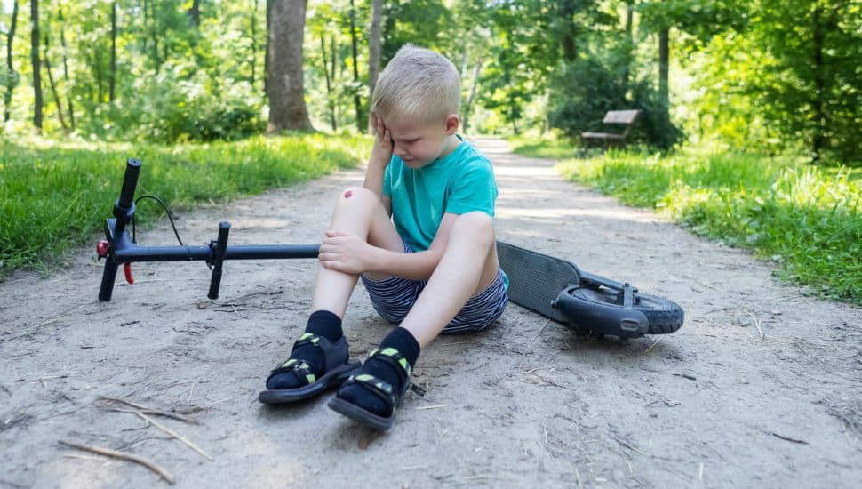A little boy without protective gear rubs his head after falling off an e-scooter.