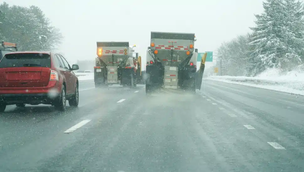 A snowplow spreads salt on the highway.