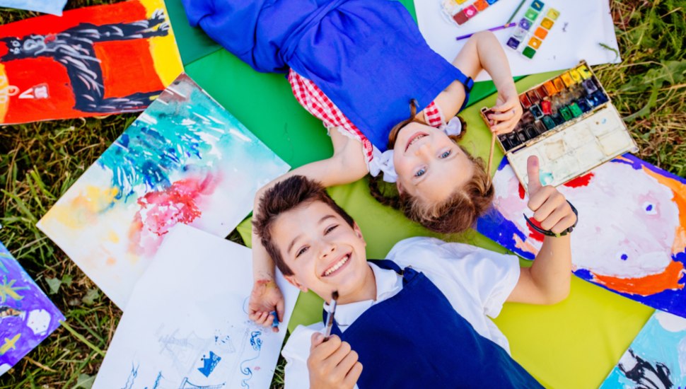 Children lie on the grass with their drawings next to them.