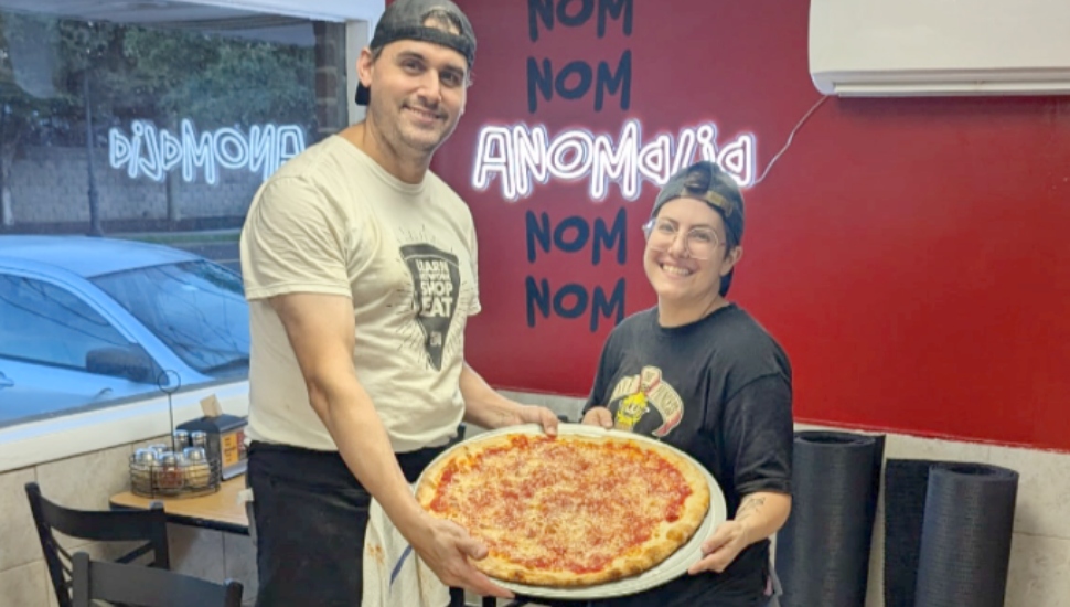 A man and a woman hold a large pizza.