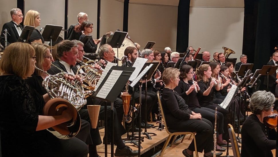 Immaculata Symphony orchestra performing on stage with musicians playing brass, woodwind, and string instruments during a concert at Alumnae Hall in Immaculata University.