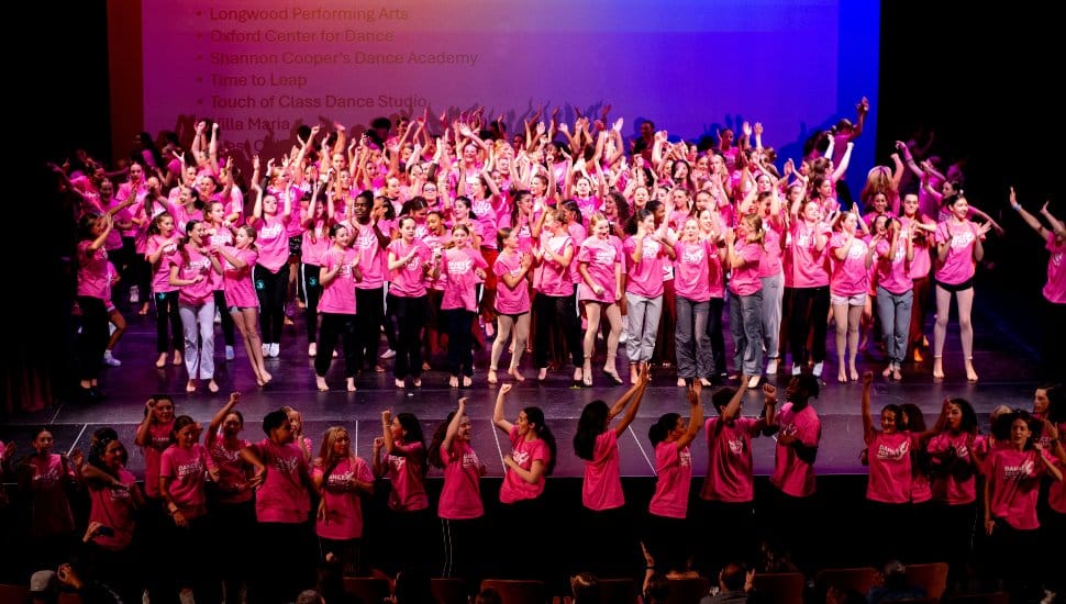 Dancers wearing pink shirts perform together on stage at West Chester University’s Dance for HER benefit concert, celebrating community and raising funds for Unite for HER in support of breast and ovarian cancer awareness.