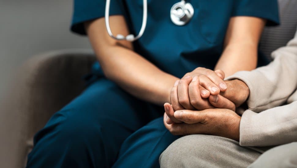 A health professional holds the hand of a patient.