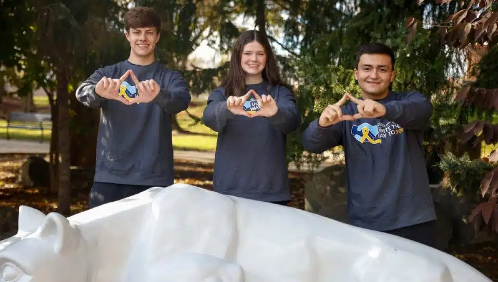 Joey Pretti, Morgan Gallagher and Charles Carlini with their hands shaped as the four diamonds logo behind the Penn State Brandywine lion statue.