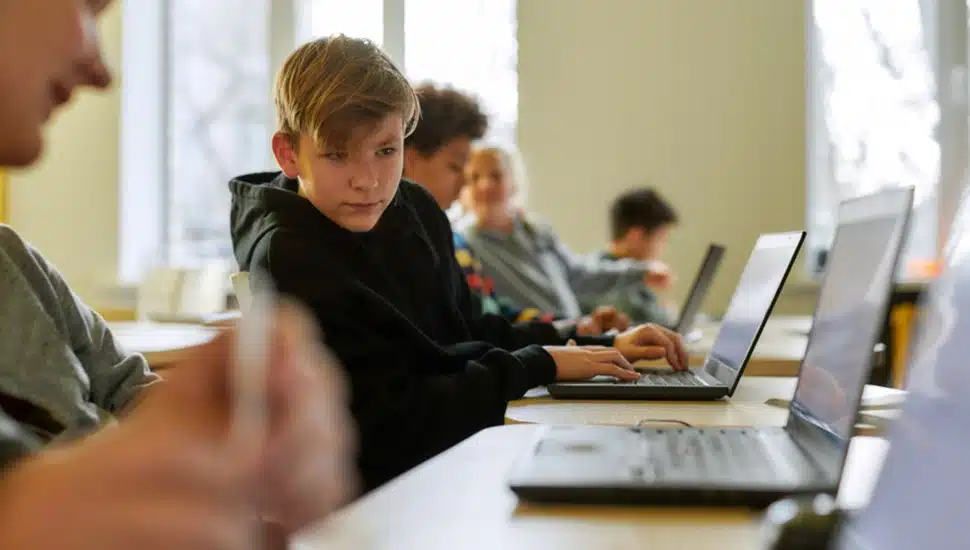 A boy sits in a group working at lap tops, staring off into space.
