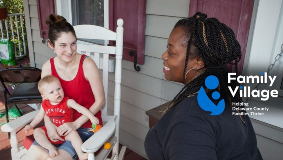 A Family Village staffer talks with a mom sitting down holding her baby.