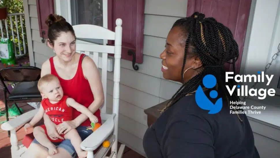 A Family Village staffer talks with a mom sitting down holding her baby.