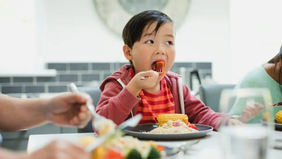 A little boy eats dinner with his family, enjoying a mouthful of vegetables.