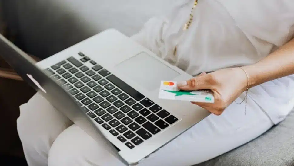 Woman holds credit card while looking at her laptop computer.