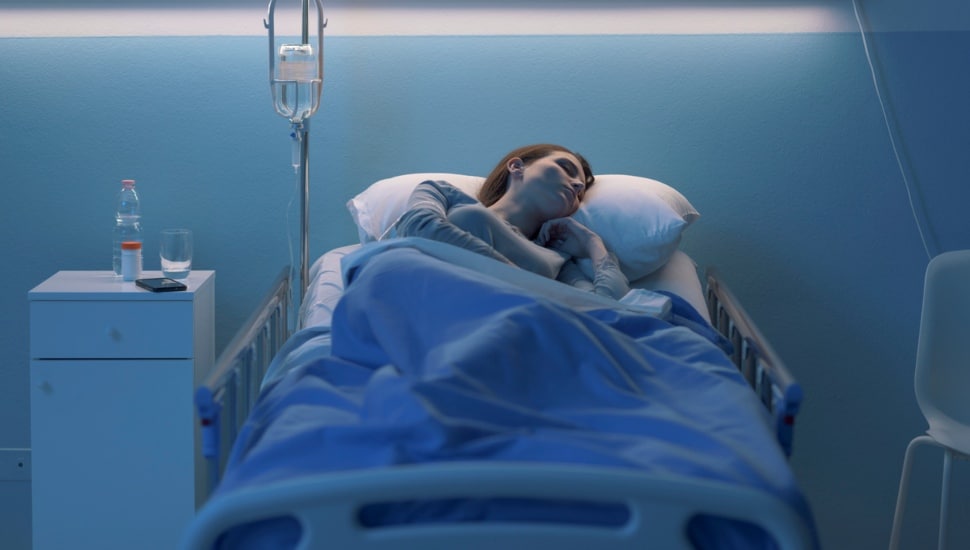 A young woman sleeps in a hospital bed at night.