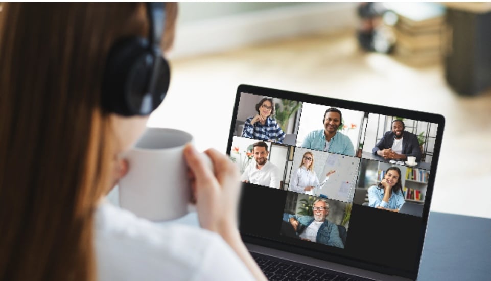 A woman enjoys a cup of coffee sitting in front of her laptop chatting with other people online.