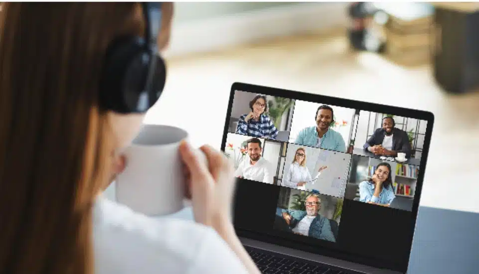 A woman enjoys a cup of coffee sitting in front of her laptop chatting with other people online.