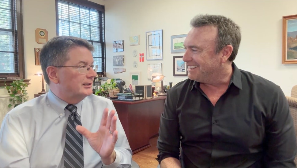 Two men speak in front of a camera.