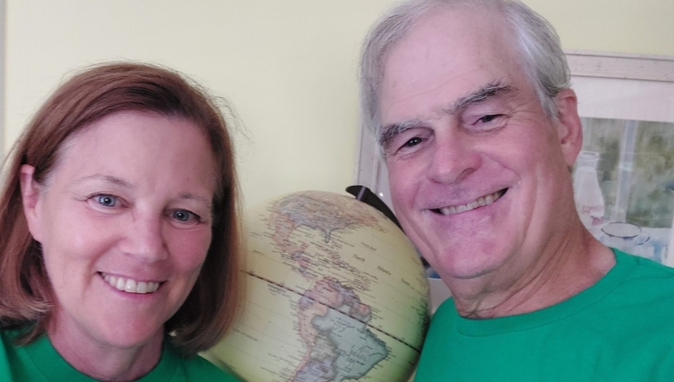 Retired man and woman smile next to a globe.