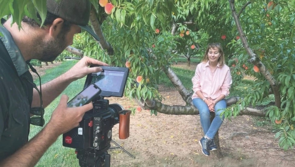 Filmmaker interviews woman sitting on tree.