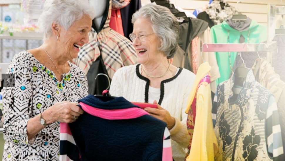 Two senior women look at some store clothes.
