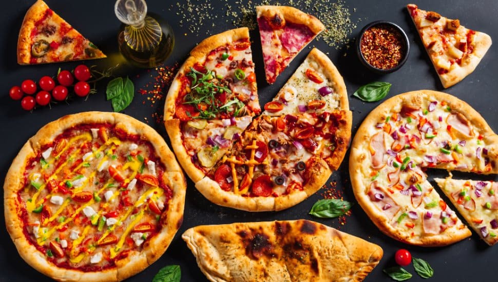 A table loaded with pizza pies and pizza slices.