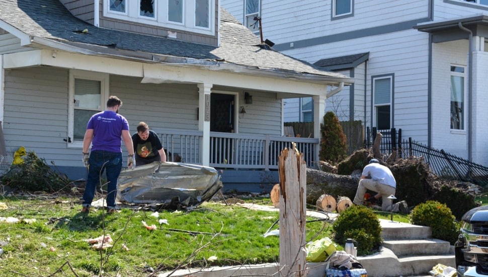 People assess property damage to house after storm.