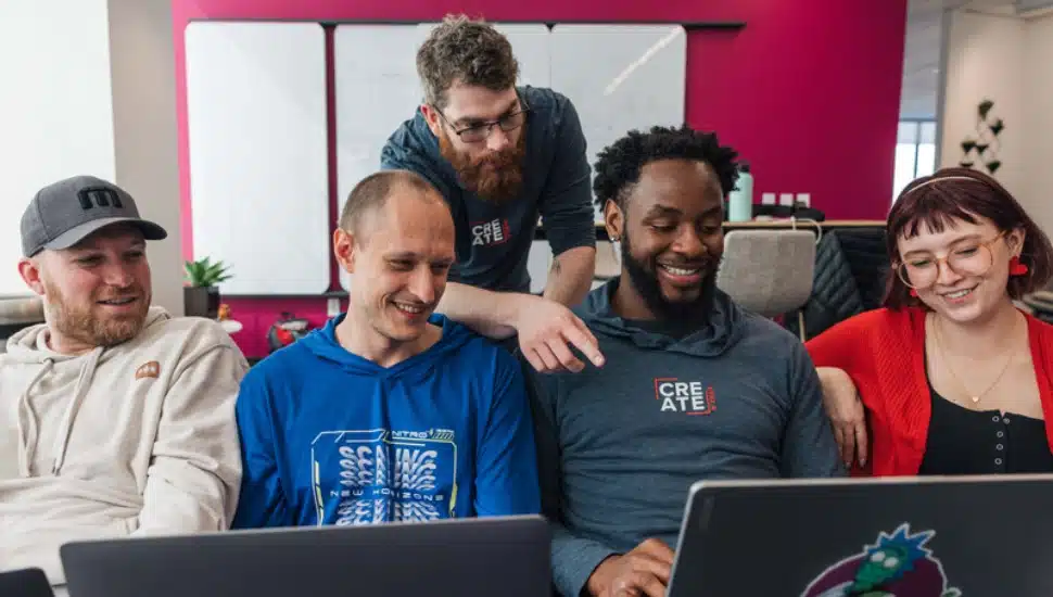 Men and women staffers are gathered around several laptop computers.