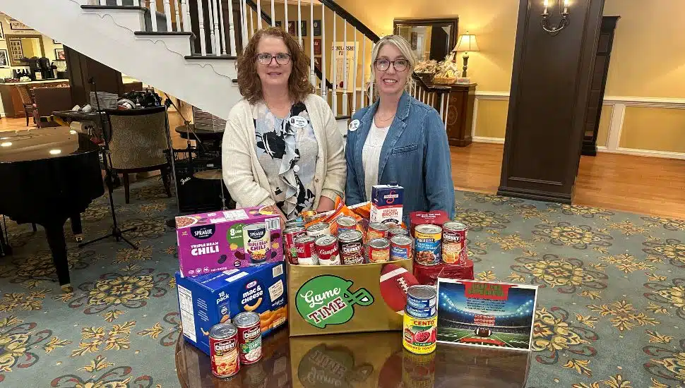 Two women stand behind some of the food items collected for the Freedom Village at Brandywine “Soup for the Super Bowl” food drive