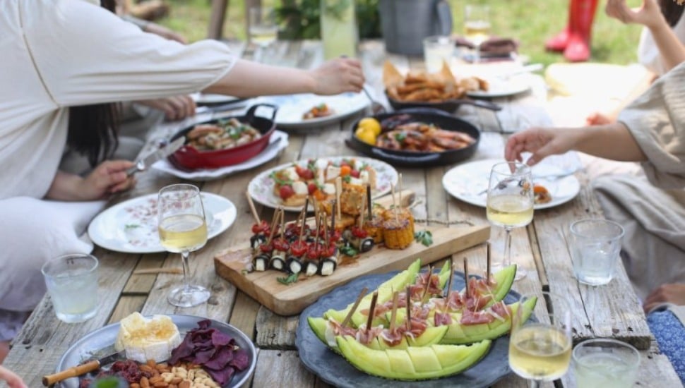 A table outside is loaded with tempting dishes as people gather around.