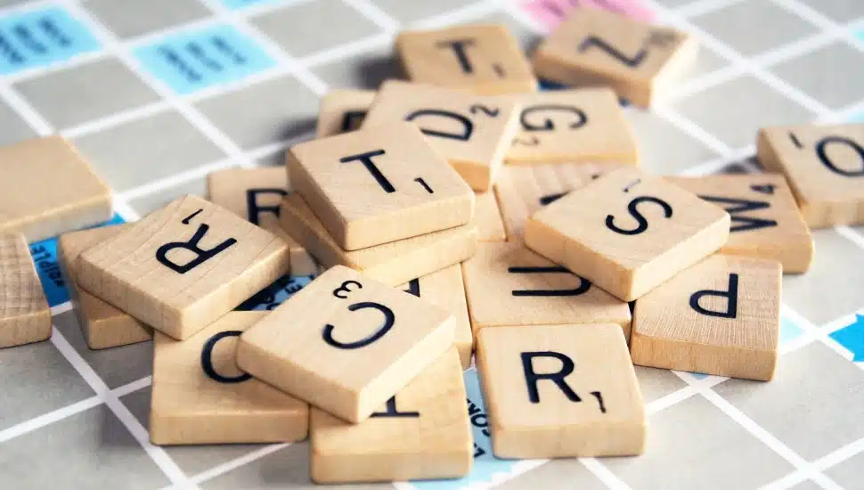 Letter tiles randomly piled on top of a Scrabble game board.