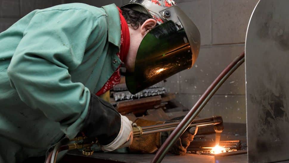 Student wearing protective gear welds metal during hands-on training in a Delaware County Community College workforce development program.