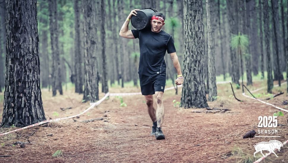 Jason Sheehan carries a heavy sandbag through a wooded Spartan obstacle course during the 2025 season competition.