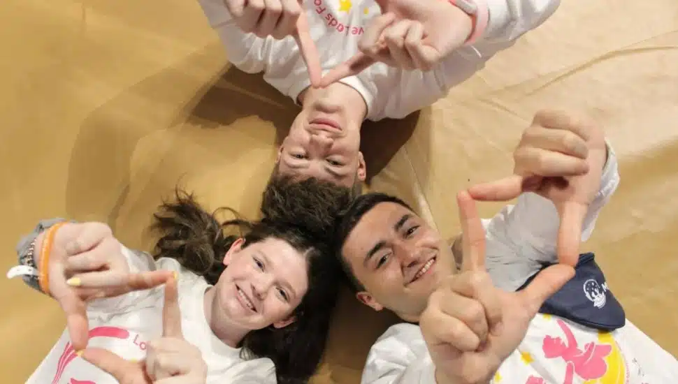Three Penn State Brandywine students, Students Charles Carlini, Morgan Gallagher, and Joey Pretti, lying in a circle on the floor.