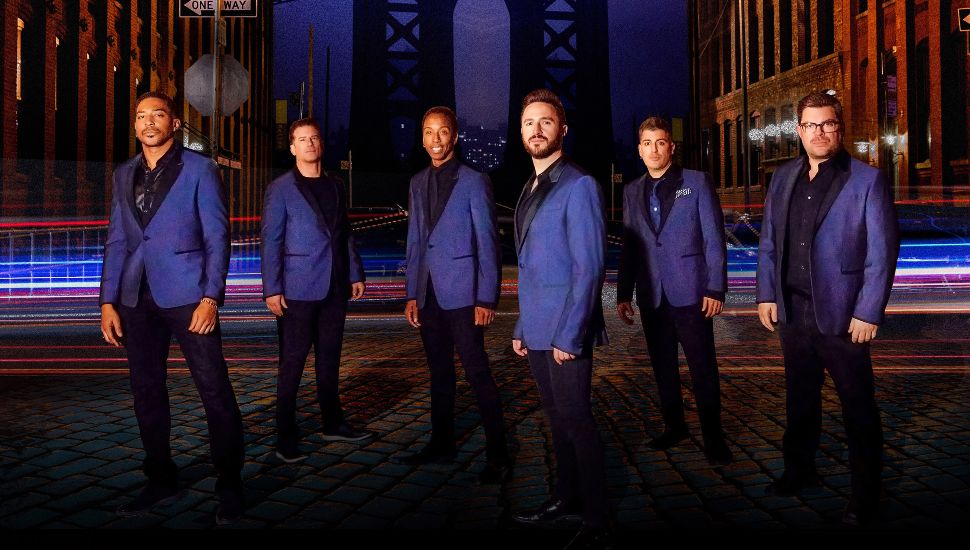 The Doo Wop Project members standing on stage dressed in matching suits.