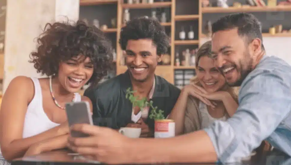 Four young men and women laughing as they look at an image on a phone.