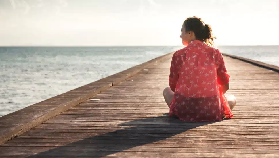 A teen girl sitting on a dock staring out at the ocean.