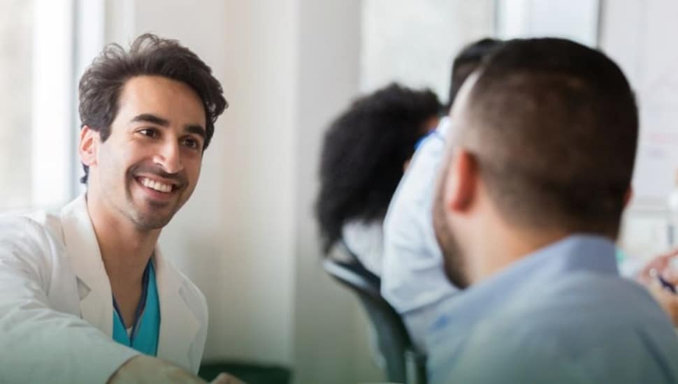 Two young male medical sales professionals shake hands.