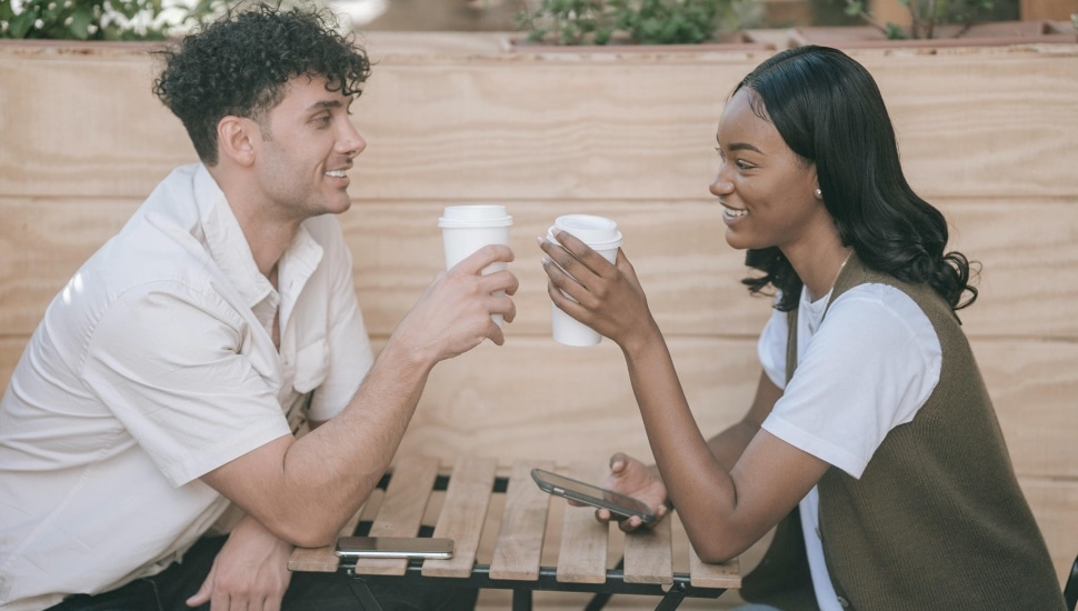 Young couple smile at each other while drinking coffee.