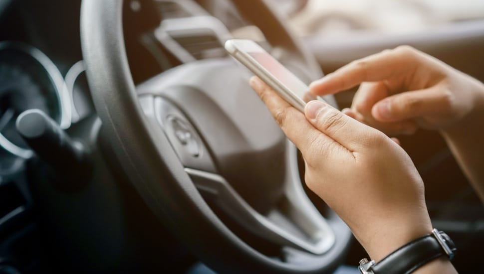 Hand holding phone in front of steering wheel.