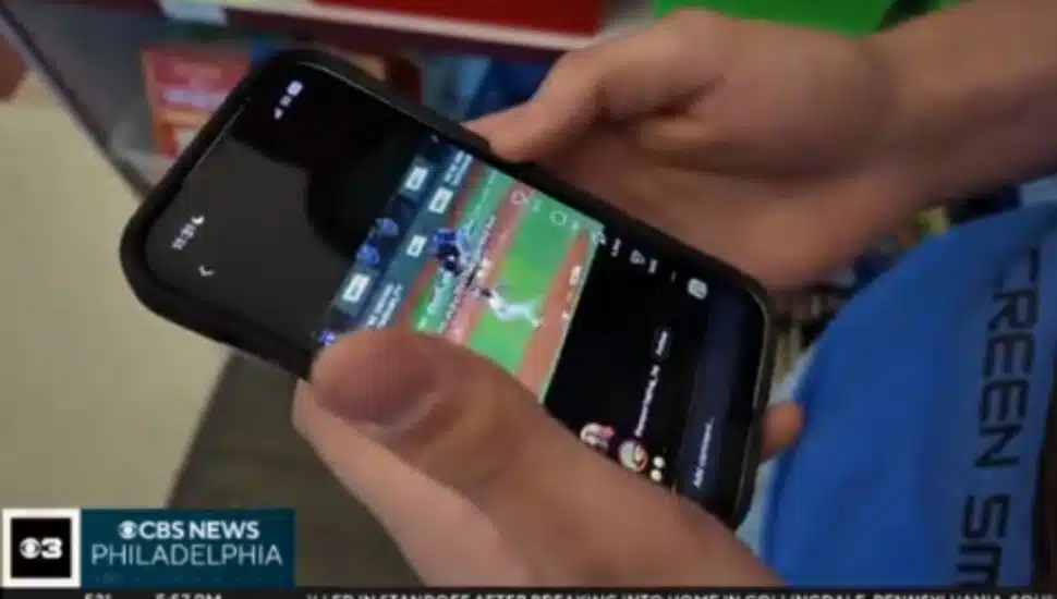 A student looks at a sporting event on their cell phone.