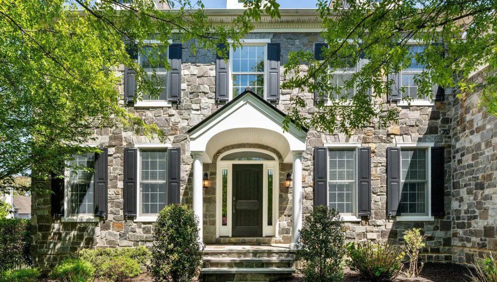 Stone house with black shutters, partially hidden behind trees.