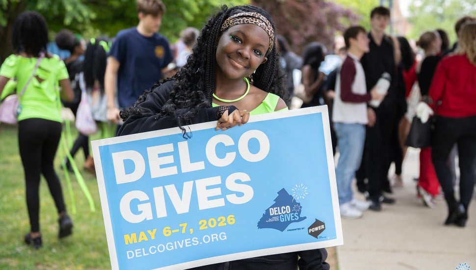 A young woman holds a Delco Gives 2026 sign.