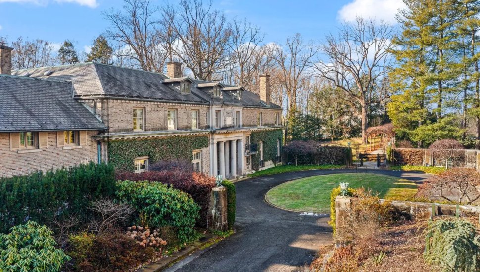 An Italianate-style mansion surrounded by shrubbery and a round driveway.