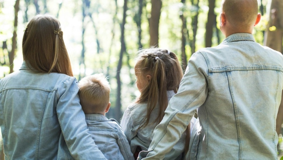 Family sits together in a forest and admires the sun.