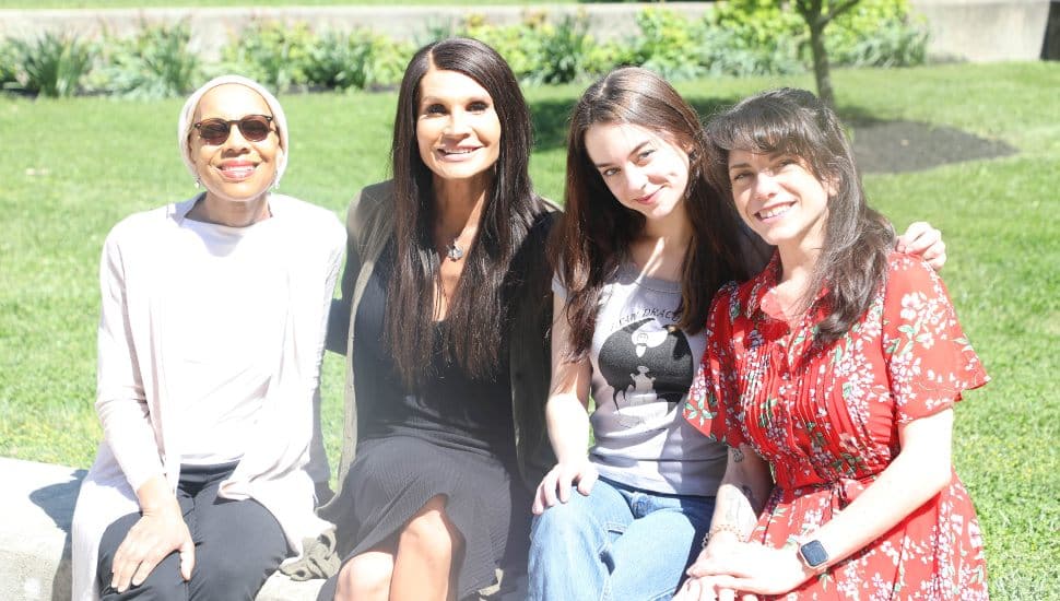 CCC Professor Tanya Gardner and students Taya Vietro, Paulina Jaus, and Katy Gallagher sit together outdoors on a sunny day on the Delaware County Community College campus.