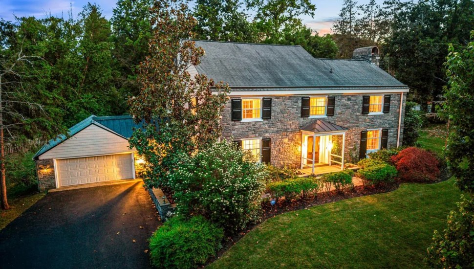 Stone colonial with black shutters surrounded by trees.